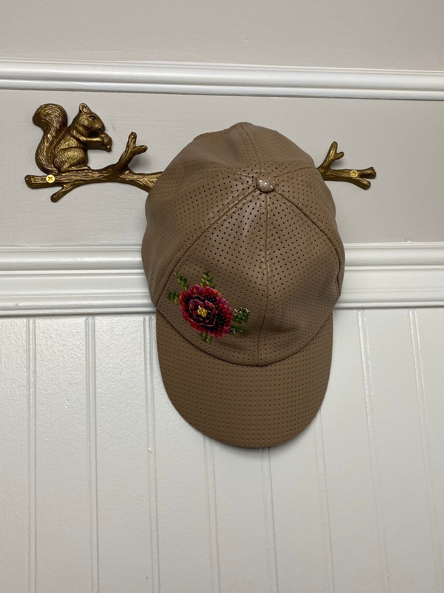 Tan perforated cap with floral cross stitched motif.
