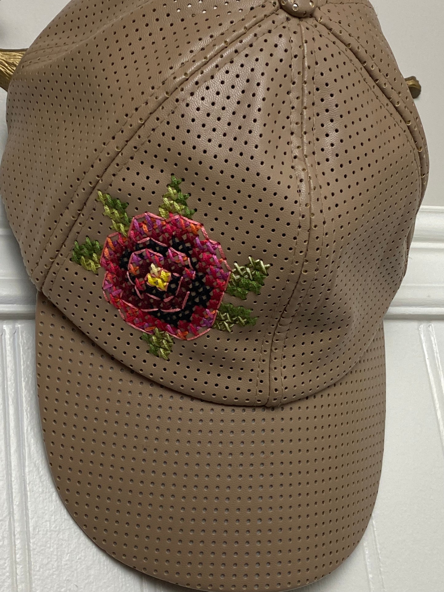 Tan perforated cap with cross stitched rose motif.