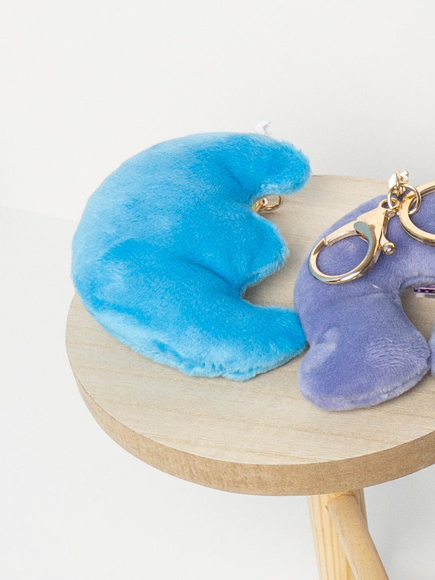 Close-up of plush sky blue crescent moon bag charm showing soft texture and gold clover charm