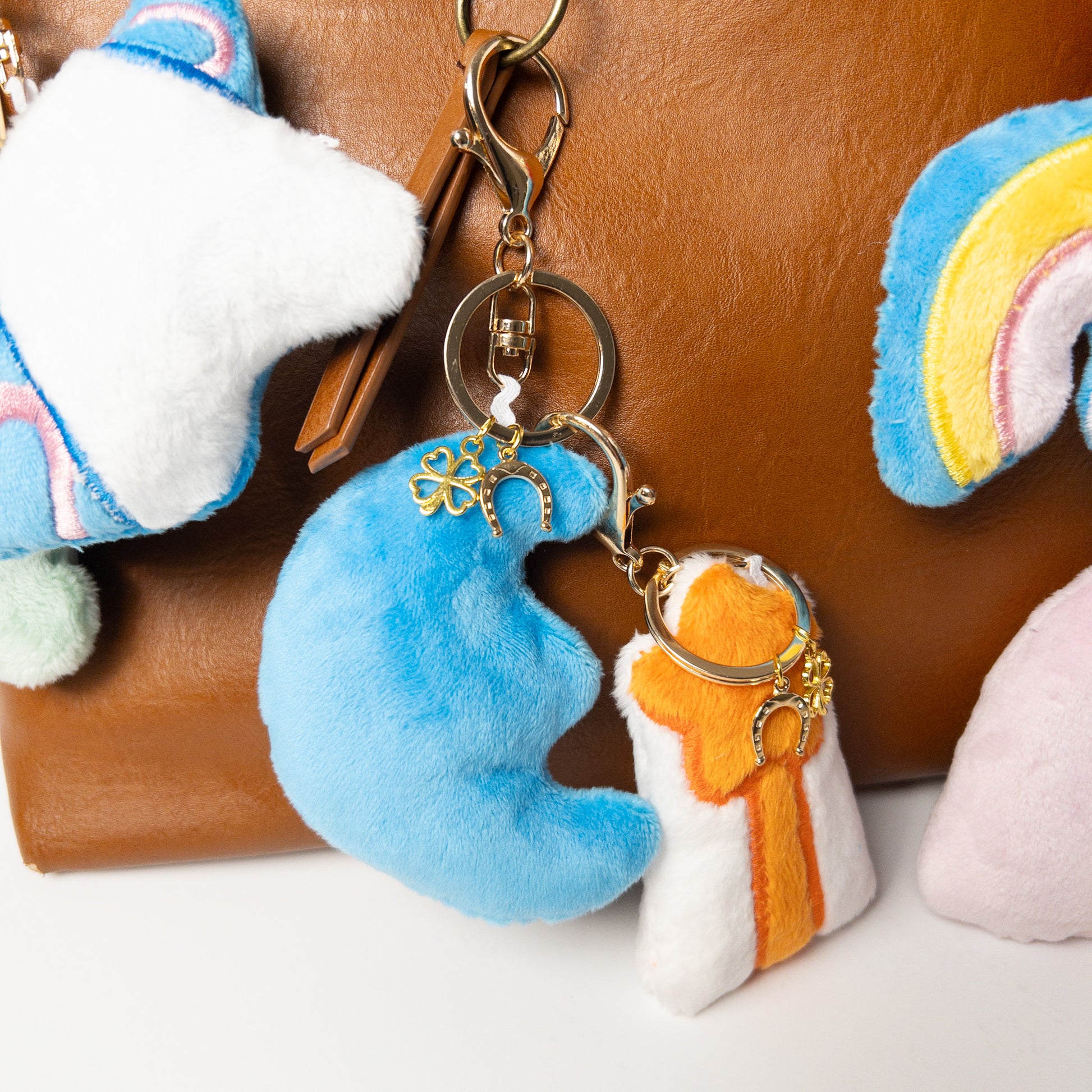 Close-up of plush blue crescent moon bag charm, highlighting small gold four-leaf clover and horseshoe charms attached