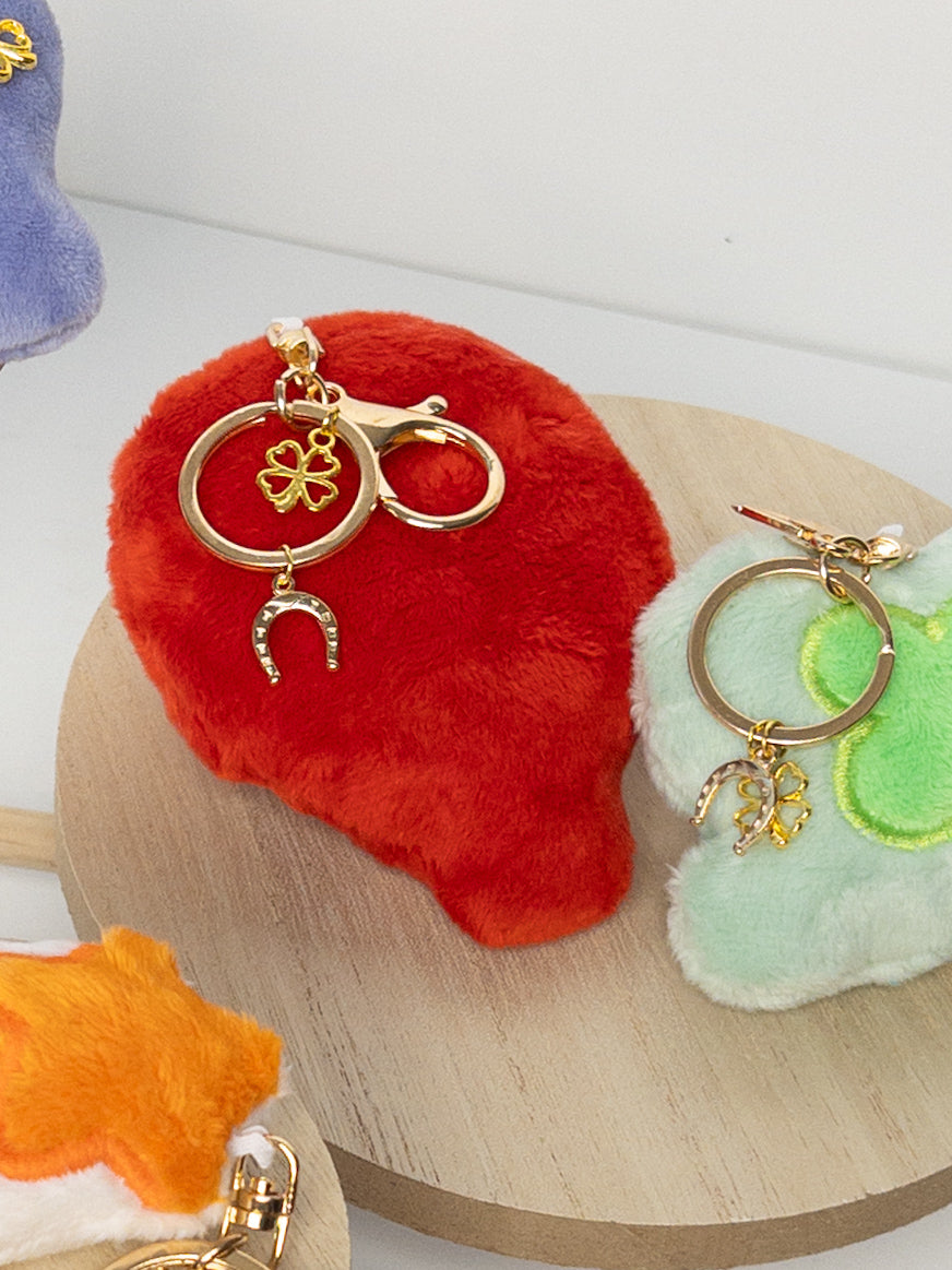 Closeup of bright red plush balloon bag charm with gold hardware, clover and horseshoe accent charms