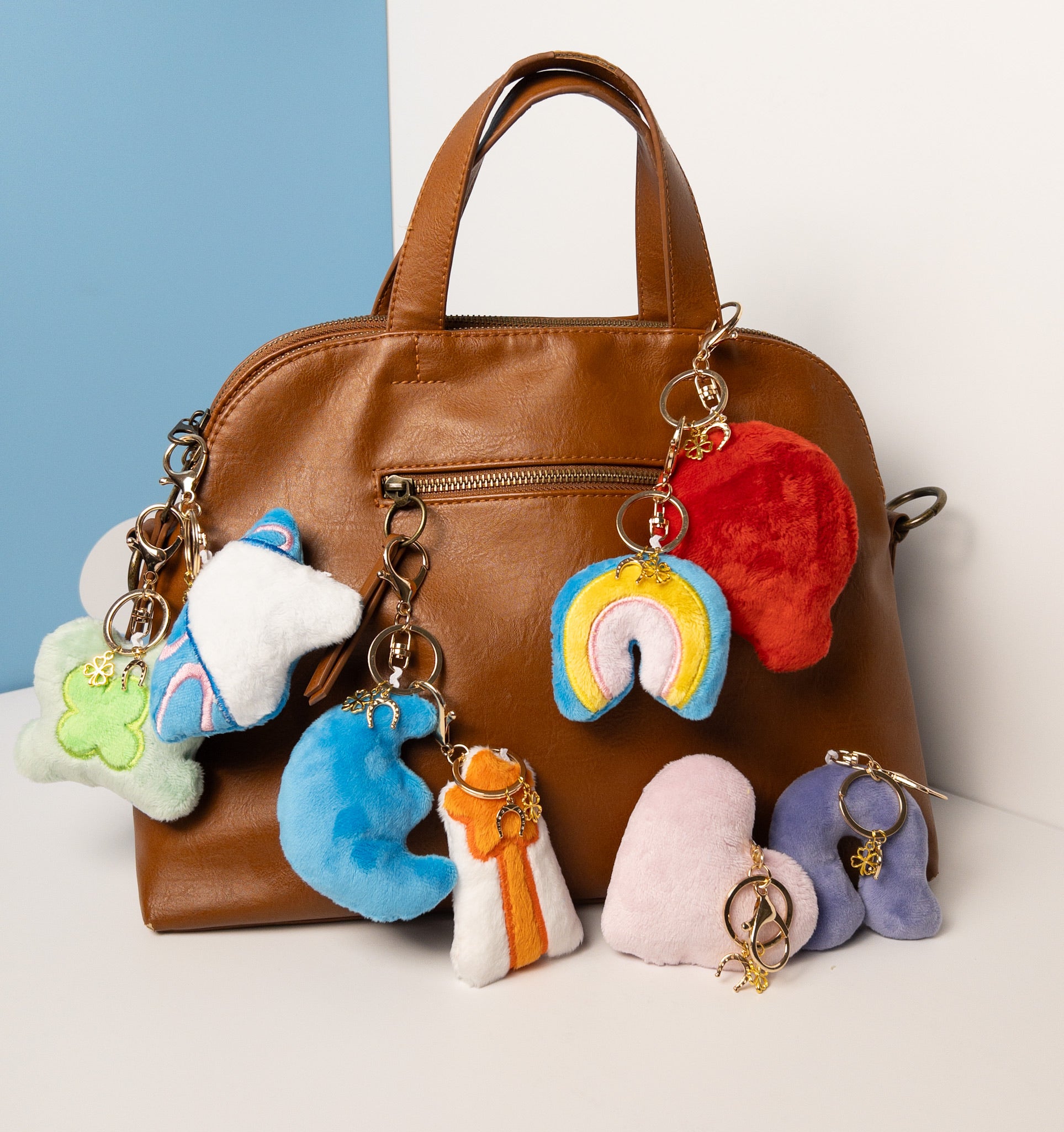 Complete collection of plush rainbow keychains in various color combinations attached to a stylish brown leather purse