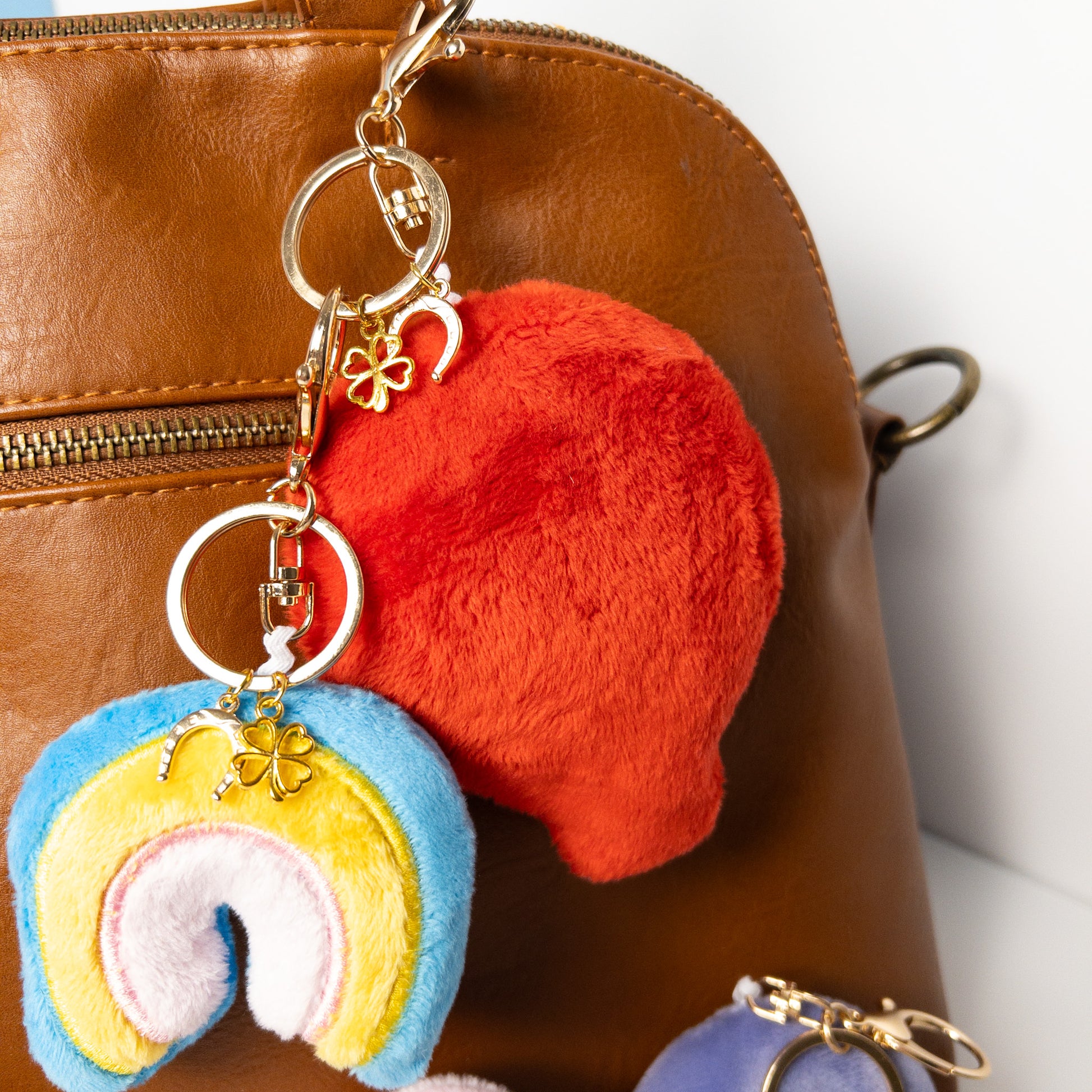 Assortment of colorful plush balloon bag charms including bright red lucky charm displayed on a brown leather handbag