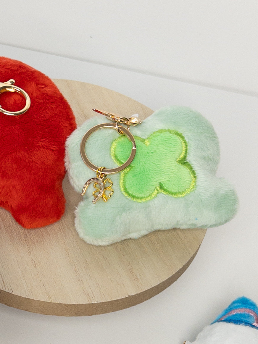 Mint green plush four-leaf clover hat bag charm with bright green clover design and gold horseshoe charm on wooden surface