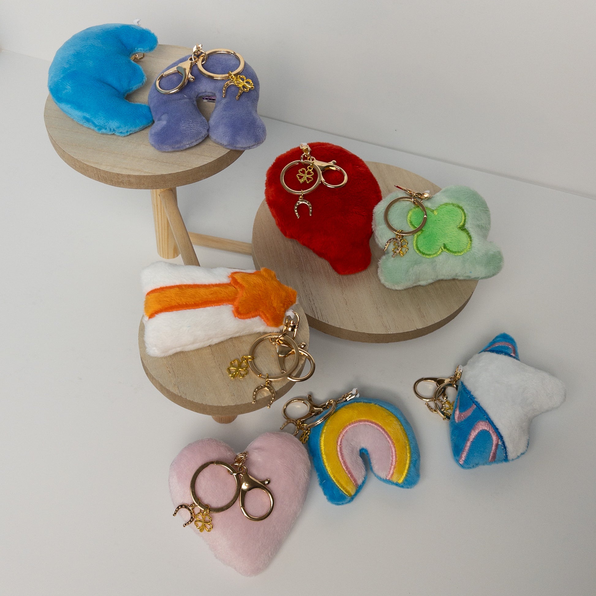 Flat lay of colorful plush bag charms collection featuring various shapes including blue crescent moon, rainbow, and other playful designs