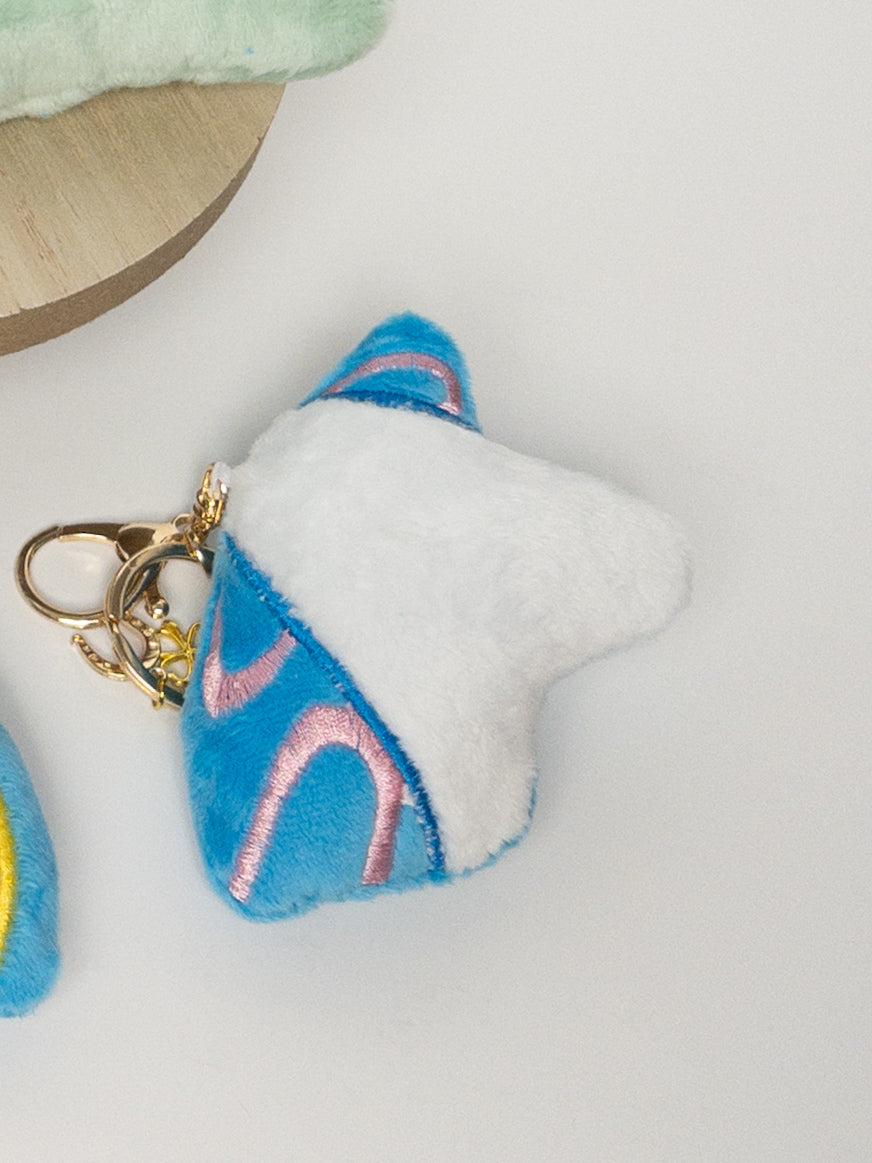 Closeup of white plush unicorn bag charm with pink and blue accents, gold hardware, and mini rainbow charm