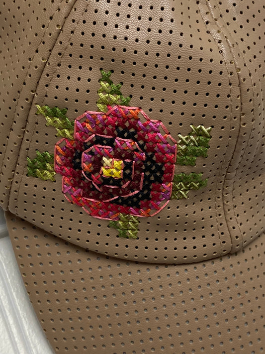 Close-up of a hand-stitched cross stitch rose on a tan perforated baseball cap